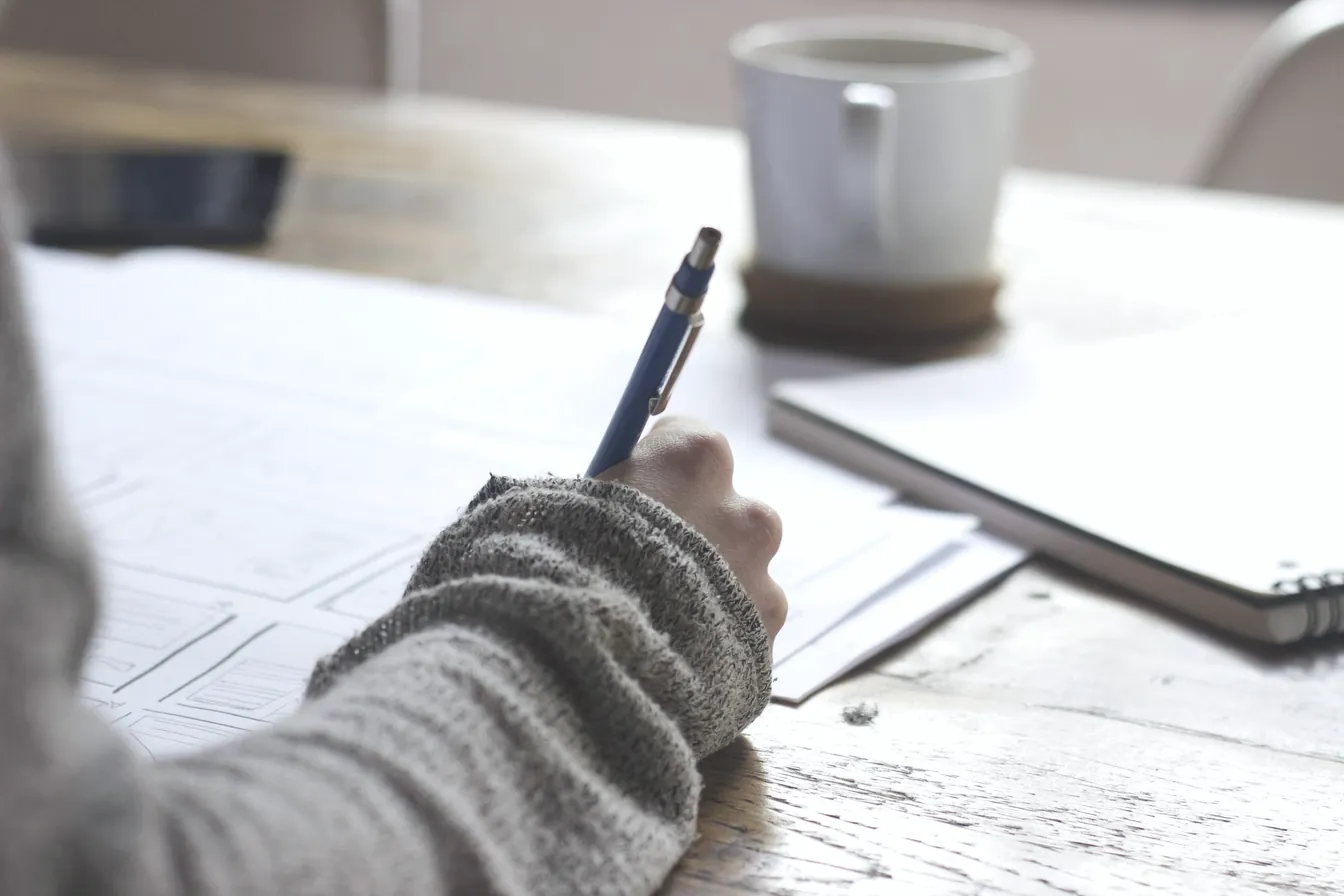 Une main écrit dans un carnet, à côté d'une tasse de café.