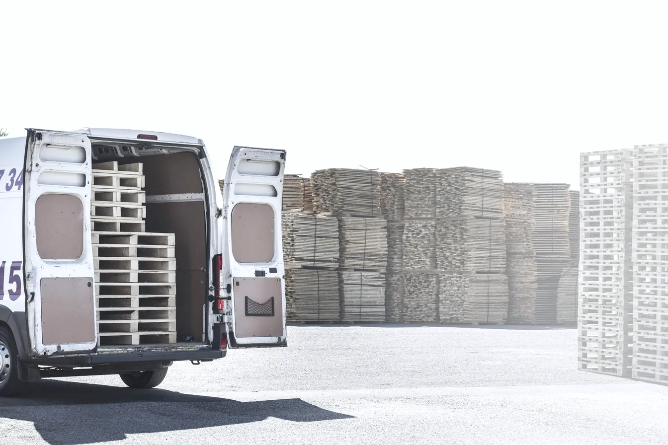 Utilitaire de livraison ouvert devant des piles de palettes.